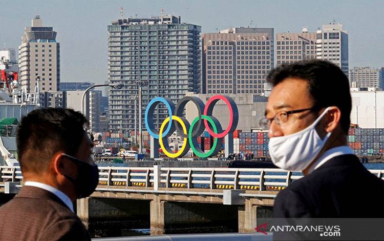 Pria-pria yang mengenakan masker wajah menyaksikan cincin raksasa Olimpiade, yang sementara diturunkan pada bulan Agustus untuk pemeliharaan di tengah wabah penyakit coronavirus (COVID-19), diangkut untuk dipasang kembali di area tepi laut di Taman Laut Odaiba di Tokyo, Jepang Desember 1, 2020. REUTERS / Kim Kyung-Hoon / File Foto. (REUTERS/Kim Kyung Hoon)