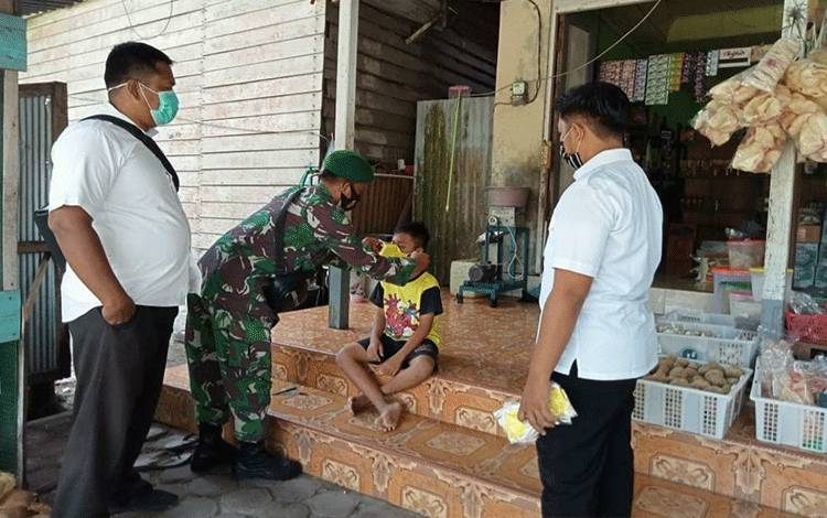 Babinsa Madurejo anggota Koramil 1014 - 01/Arsel Serda Suharyanto saat memberikan masker pada anak yang kedapatan tidak memakai masker.