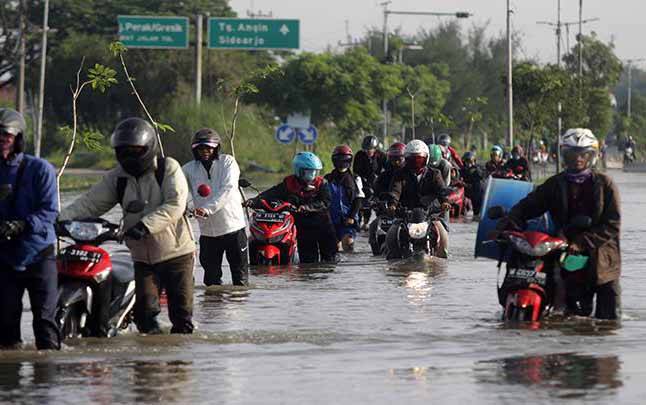 Pengendara mendorong sepeda motor menerobos banjir yang menggenangi jalan raya Porong, Sidoarjo, Jawa Timur, Selasa 16 Februari 2021. Curah hujan yang tinggi sejak Senin (15/2) malam mengakibatkan banjir yang merendam jalan raya Porong sehingga mengganggu kelancaran transportasi umum. (foto : ANTARA FOTO/Umarul Faruq)