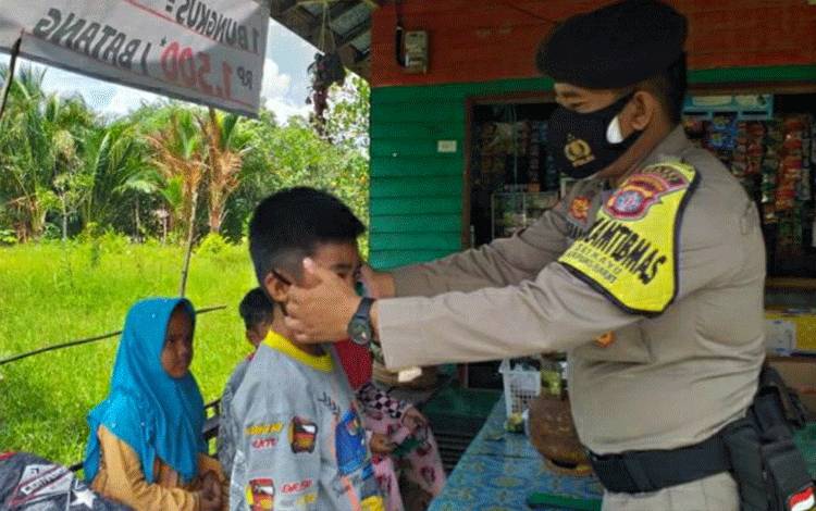 Personel Polsek Kapuas Barat Bripka Misrani saat memberikan masker kepada sejumlah anak-anak di Desa Sei Kayu.