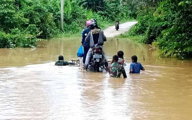 Babinsa Koramil 1013-01 Kandui membantu warga untuk penyebrangkan kendaraanyang akan melintasi akses jalan yang terputus akibat banjir, Jumat 26 Maret 2021