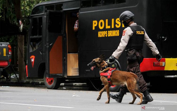 Anggota polisi berjalan dengan anjing pelacak saat mengumpulkan sisa serpihan ledakan bom bunuh diri di depan Gereja Katedral Makassar, Sulawesi Selatan, Senin (29/3/2021). Kepolisian masih melakukan olah TKP serta mengumpulkan serpihan sisa ledakan pada hari kedua pascaledakan bom bunuh diri yang terjadi pada Minggu (28/3/2021) di depan gereja tersebut. ANTARA FOTO/Arnas Padda/yu/hp.