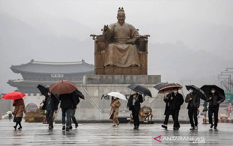 Para pejalan kaki memakai masker dan payung saat berjalan di bawah rintik hujan, di tengah pandemi virus corona (COVID-19), di pusat kota Seoul, Korea Selatan, Kamis (19/11/2020). ANTARA FOTO/REUTERS/Heo Ran/NZ/djo/am.