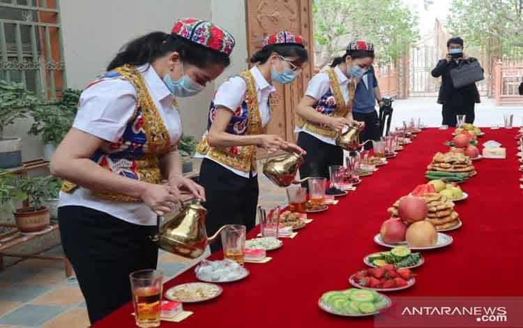 Sekelompok perempuan dari etnis minoritas Muslim Uighur di Yiganqi, Kota Aksu, Daerah Otonomi Xinjiang, China, menuangkan minuman teh untuk para tamu, Selasa (20/4/2021)