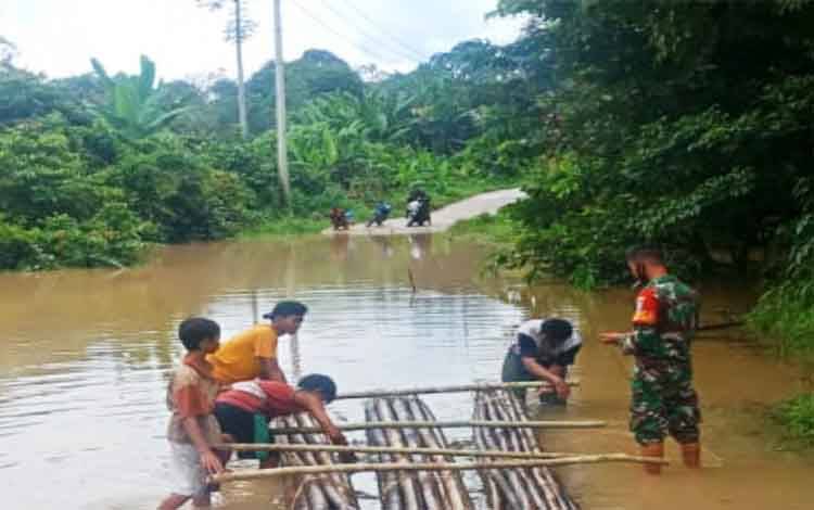 Babinsa Koramil 1013-01 Kandui membantu membuat rakit untuk bagi warga akan menyeberangi genangan air di jalan terendam banjir