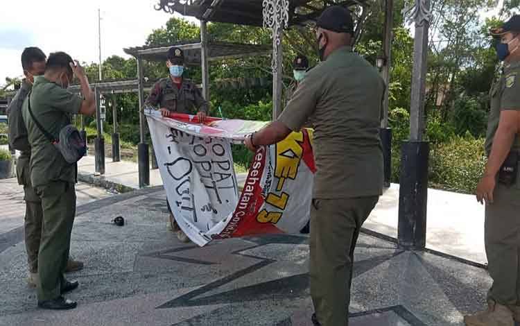 Petugas saat menurunkan spanduk provokatif protes Covid-19 di Palangka Raya, Selasa 13 Juli 2021