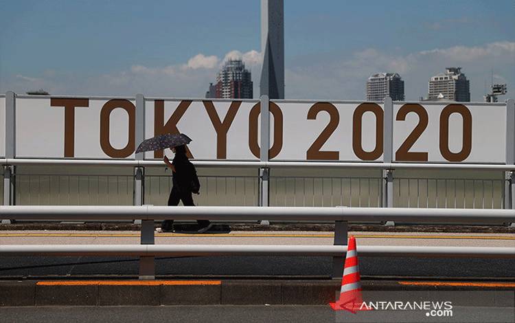 Seorang perempuan berjalan di bawah payung melintasi papan tanda Olimpiade Tokyo di Tokyo, Jepang, Senin (19/7/2021). ANTARA/REUTERS/Thomas Peter/am.