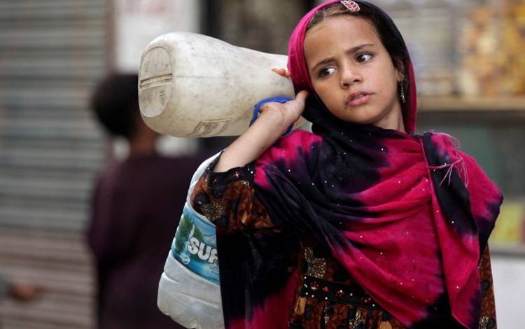 Seorang anak perempuan pengungsi Afghanistan membawa botol untuk diisi dengan air di Lahore, Pakistan, Juni 2019