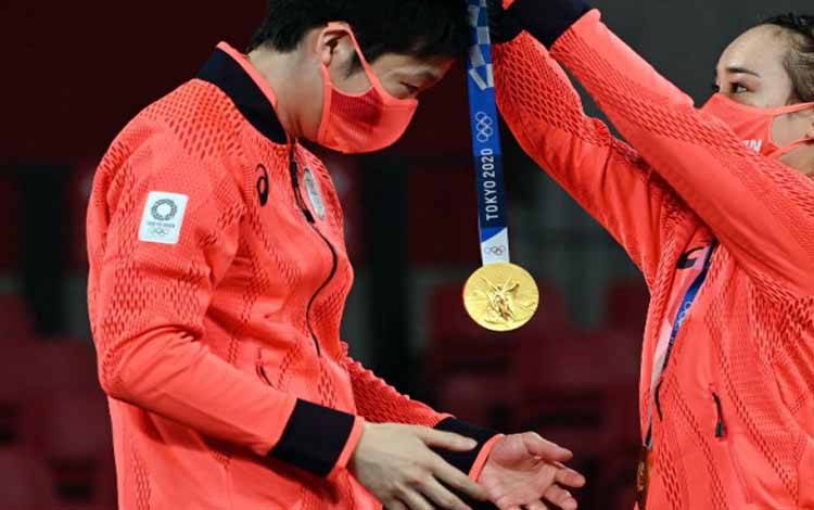 Petenis meja putra Jepang Jun Mizutani dikalungi medali emas oleh mitranya dalam ganda campuran, Mima Ito, di podium setelah mereka memenangkan medali emas ganda campuran tenis meja Olimpiade Tokyo di Tokyo Metropolitan Gymnasium, 26 Juli 2021