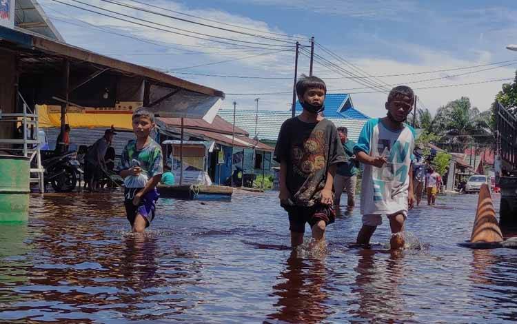 Anak-anak sedang berjalan melintasi genangan banjir di salah satu wilayah di Kalteng