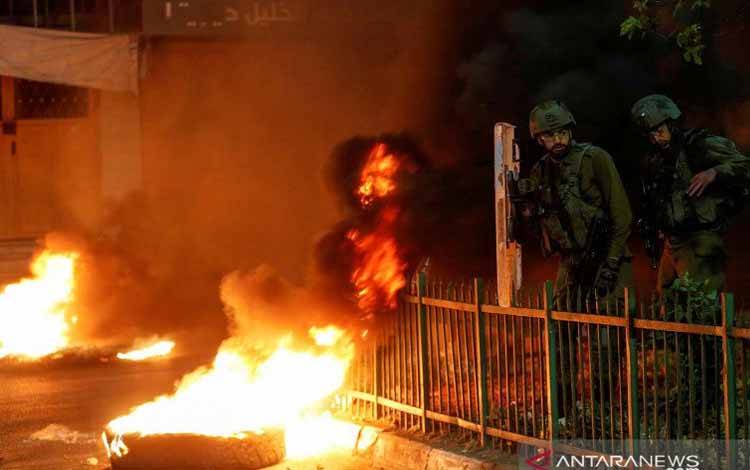Tentara Israel berdiri di samping pembakaran ban saat warga Palestina mengambil bagian dalam protes anti-Israel atas ketegangan di Yerusalem, di Hebron di Tepi Barat yang diduduki Israel, Senin (26/4/2021)