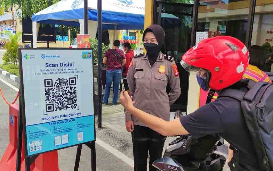 Pengunjung mencoba scan barcode aplikasi PeduliLindungi di pintu masuk Polresta Palangka Raya.