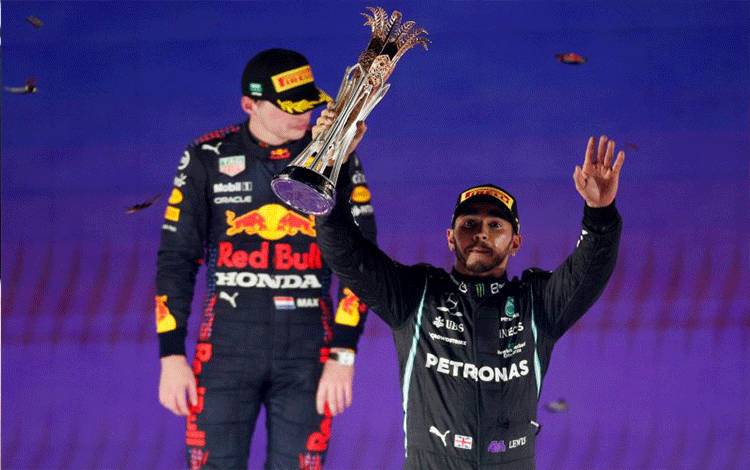 Pebalap Mercedes Lewis Hamilton merayakan kemenangan bersama trofi di podium setelah menjuarai balapan Grand Prix F1 Arab Saudi di Sirkuit Corniche Jeddah, Minggu (5/12/2021), sementara pebalap Red Bull Max Verstappen yang berada di tempat kedua menyaksikan. (REUTERS/HAMAD I MOHAMMED)