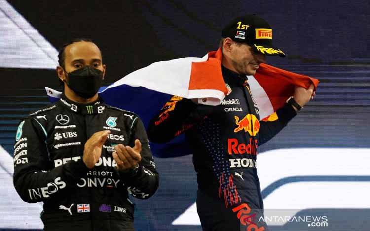 Pembalap Red Bull Max Verstappen merayakan kemenangan balapan dan kejuaraan dunia dengan bendera Belanda di podium saat pebalap Mercedes Lewis Hamilton terlihat setelah finis kedua selama Grand Prix Abu Dhabi di Sirkuit Yas Marina, Abu Dhabi, Uni Emirat Arab, Minggu (12/12/2021).