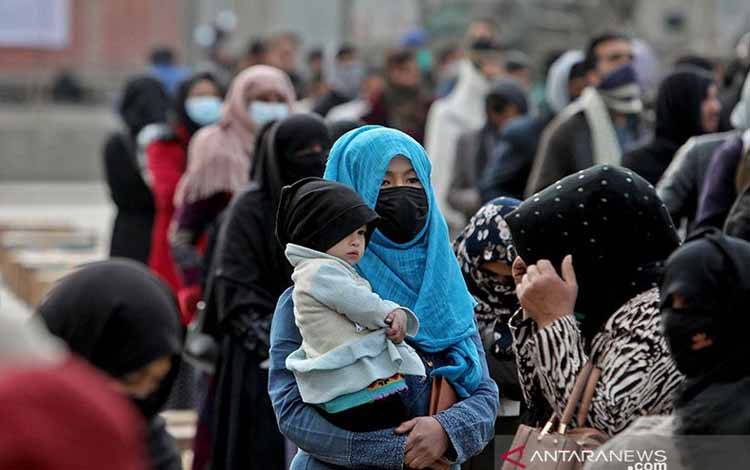 Seorang peremppuan Afghanistan menggendong anaknya di tengah orang-orang yang menunggu paket bantuan yang disalurkan oleh sebuah kelompok bantuan kemanusiaan Turki di sebuah pusat penyaluran bantuan di Kabul, Afghanistan, Rabu (15/12/2021)