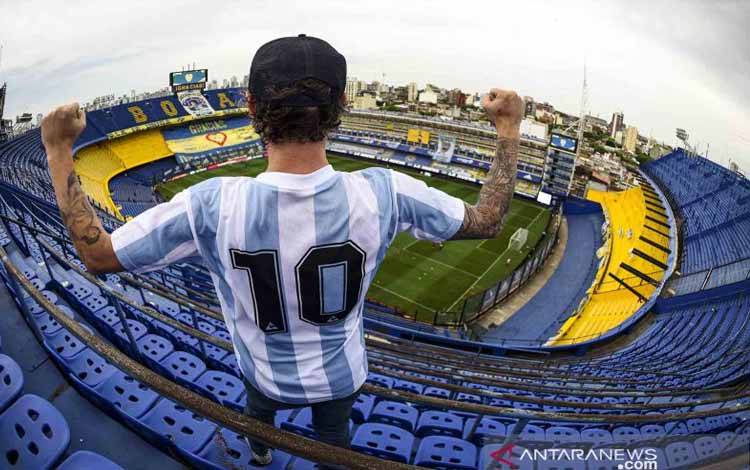 Seorang pendukung berfoto dengan memakai jersey dari mendiang legenda sepak bola Diego Maradona bernomor punggung 10 sebelum pertandingan Copa Diego Maradona antara Boca Juniors melawan Newell's Old Boys di Stadion La Bombonera, Buenos Aires, Argentina, Senin (30/11/2020) dini hari