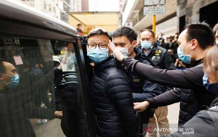 Penjabat pemimpin redaksi Stand News Patrick Lam, salah satu dari enam orang yang ditangkap atas dugaan "konspirasi menerbitkan publikasi yang menghasut" menurut Kepolisian Hong Kong, dikawal oleh polisi usai penggeledahan kantornya di Hong Kong (29/12/2021)