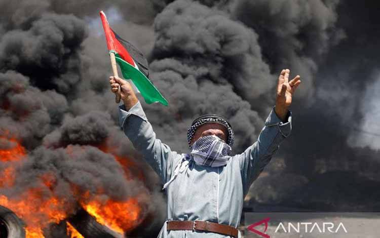 Seorang pria memegang bendera Palestina selama protes terhadap aktivitas pemukiman Israel di Kafr Qaddum di Tepi Barat yang diduduki Israel (1/7/2022). ANTARA FOTO/REUTERS/Raneen Sawafta/aww