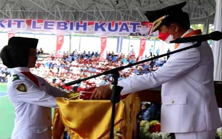 Bupati Barito Utara, Nadalsyah menyerahkan bendera pusaka merah putih kepada pembawa bendera Paskibraka di arena terbuka Tiara Batara Muara Teweh, Rabu 17 Agustus 2022