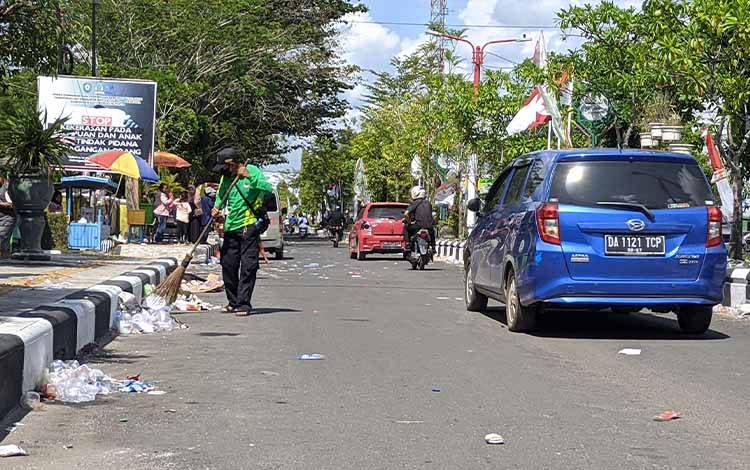 Seorang petugas kebersihan saat menyapu sampah yang berserakan di Jalan A Yani, usai pawai pembangunan. (FOTO: HAMIM)