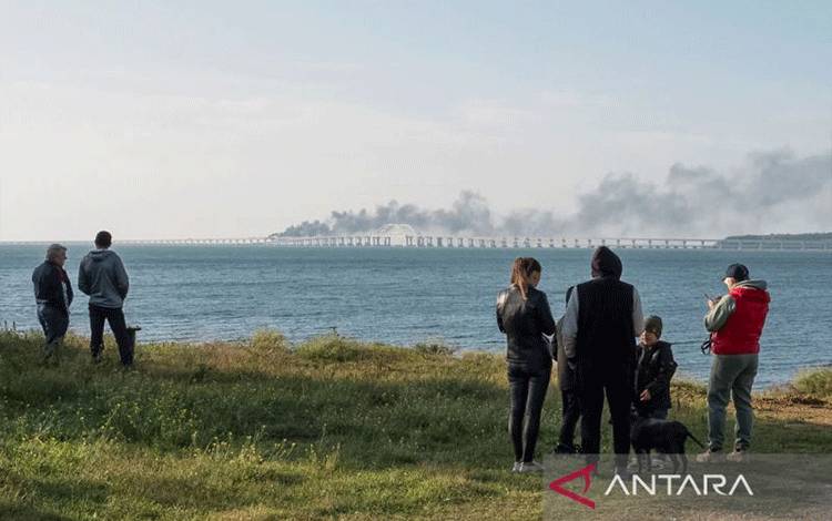 Orang-orang menyaksikan Jembatan Kerch yang terbakar usai ledakan di Selat Kerch, Krimea, 8 Oktober 2022. (ANTARA/REUTERS/Stringer/as)
