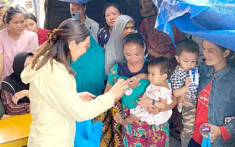 Monica Puteri Rasyid (jaket kuning) memberikan susu kepada salah satu anak korban banjir.(FOTO: TESTI PRISCILLA)