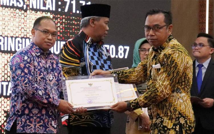 Kepala Diskominfosantik Gunung Mas Ruby Haris saat menerima piagam dan plakat penghargaan dari Komisi Informasi Kalimantan Tengah. (FOTO: DISKOMINFOSANTIK GUMAS)