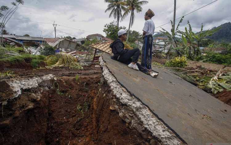 Dua orang anak berdiri dengan latar belakang rumah yang rusak akibat gempa bumi di Sarampad, Kabupaten Cianjur, Jawa Barat, Sabtu (26/11/2022). . ANTARA FOTO/Yulius Satria Wijaya/hp. (ANTARA FOTO/YULIUS SATRIA WIJAYA)