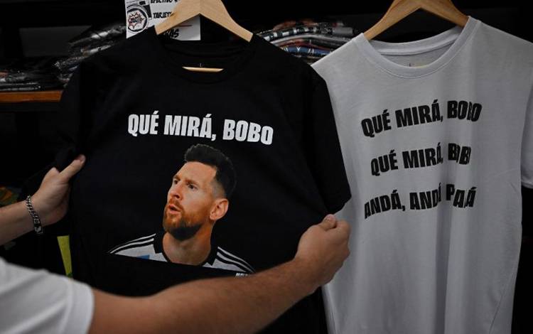 Seorang warga memegang kaus bergambarkan striker Argentina Lionel Messi dan frase yang berarti "Apa yang kau lihat, bodoh" di suatu toko di Buenos Aires, Argentina. (12/12/2022) (AFP/LUIS ROBAYO)