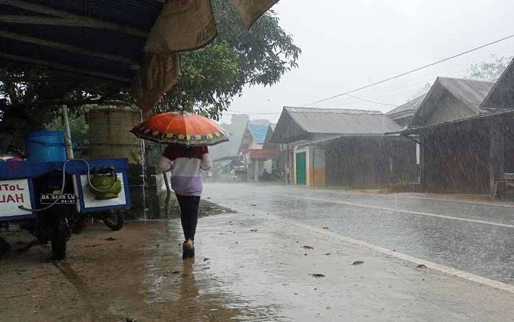 Warga menggunakan payung saat hujan lebat di Kabupaten Barito Timur. (FOTO: BOLE MALO)