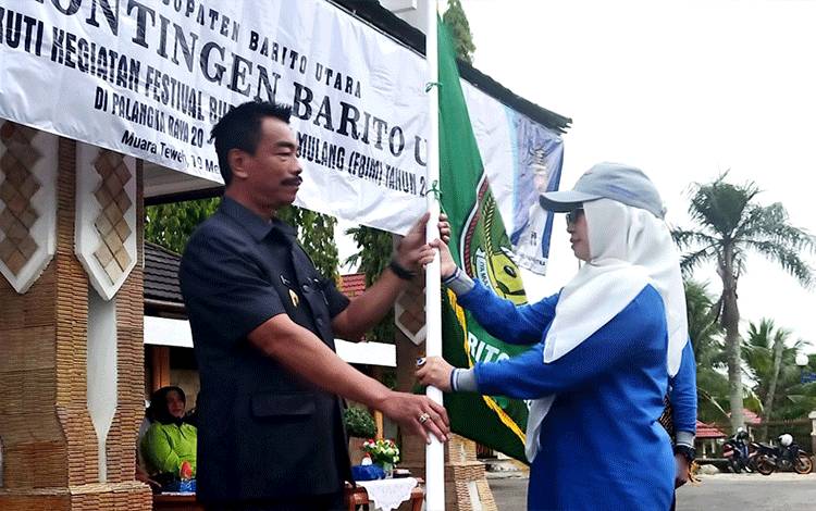 Wakil Bupati Barito Utara, Sugianto Panala Putra menyerahkan bendera lambang daerah kepada Kadis Budparpora Barito Utara, Hj Annisa Cahyawati usai pelepasan kontingen FBIM di halaman kantor bupati, Jumat 19 Mei 2023. (Foto: Dhani)