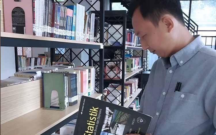 Seorang warga mengunjungi perpustakaan dan membuka buku statistik. (FOTO: DISPUSIP KALTENG)
