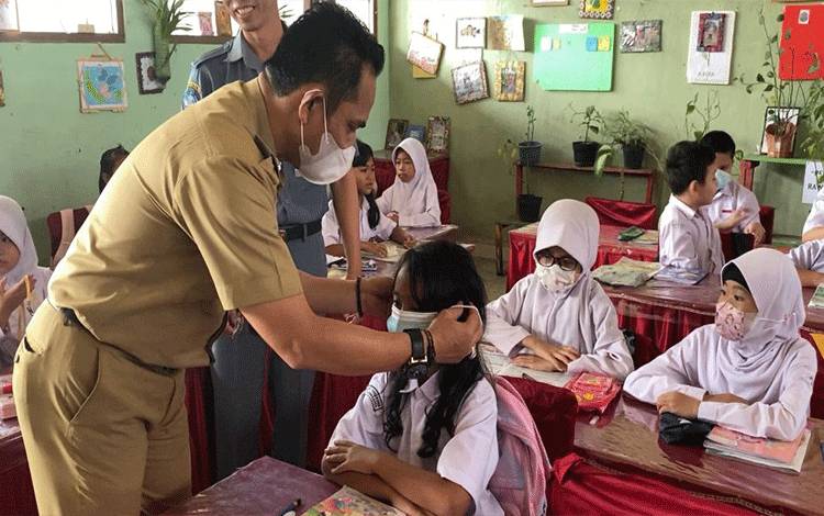 Camat Pahandut, Berlianto memasangkan masker ke murid SD. (FOTO: HENDRI)