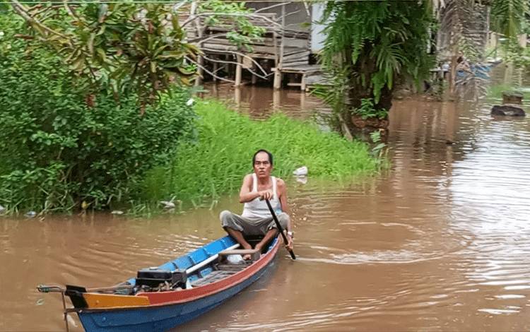 Seorang warga Kelurahan Kameloh Baru mendayung perahu di tengah permukiman yang terendam banjir (FOTO: HENDRI)