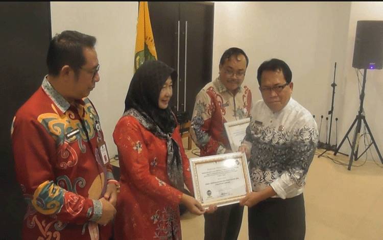 Pj Bupati Kapuas, Erlin Hardi saat serahkan piagam penghargaan pelayanan publik kepada Dinas Dukcapil Kapuas. (FOTO: IST)