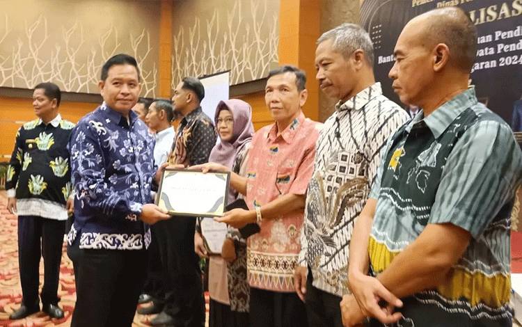 Kepala Dinas Pendidikan Seruyan Rusdi Hidayat saat menyerahkan Piagam Penghargaan kepada pihak sekolah dalam pengelolaan BOS belum lama ini (Foto : IST)